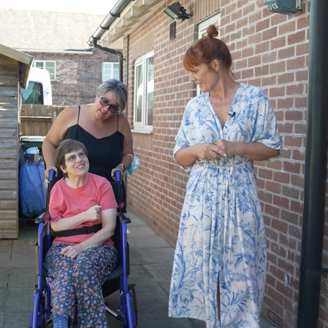 A photo of Helen Nickless, our new CEO walking and chatting with a person we support in a wheelchair and their support worker 